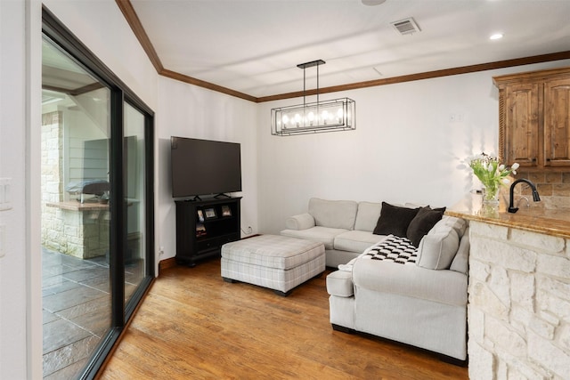 living room with crown molding, a notable chandelier, visible vents, and light wood finished floors