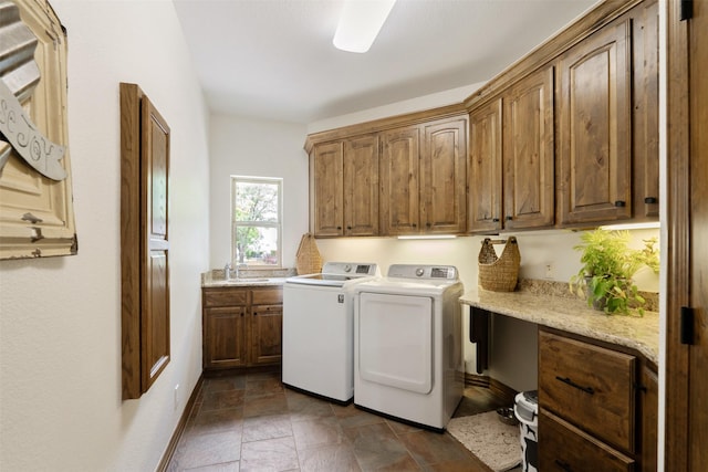 washroom featuring stone finish flooring, cabinet space, a sink, baseboards, and washer and dryer