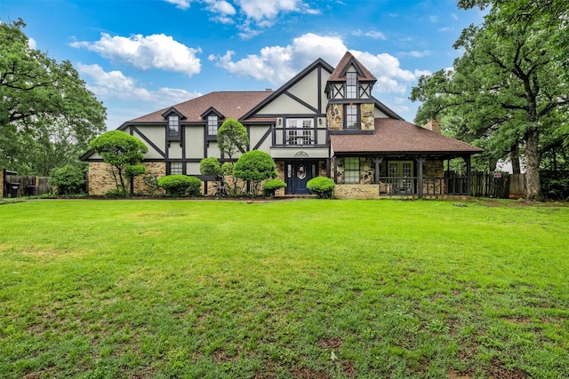 tudor home with a front lawn, stucco siding, and fence