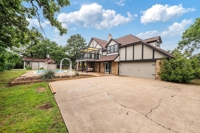 tudor-style house with a storage unit, brick siding, an outdoor pool, concrete driveway, and a balcony