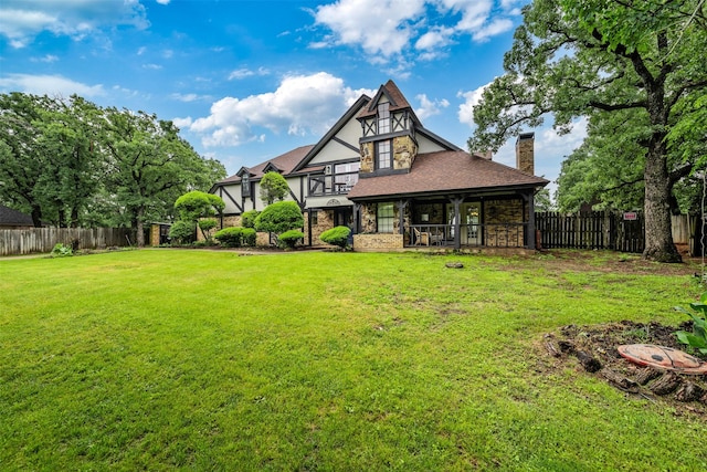 rear view of house featuring a yard, a chimney, a fenced backyard, and stone siding