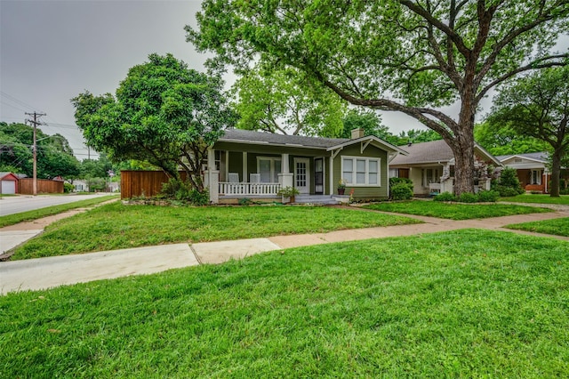 ranch-style house featuring covered porch, a front yard, and a chimney