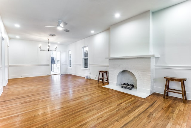 unfurnished living room with light wood-style flooring, a ceiling fan, a chandelier, a brick fireplace, and recessed lighting