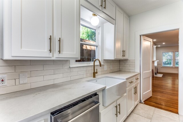 kitchen with stainless steel dishwasher, a sink, white cabinets, and healthy amount of natural light