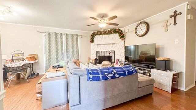 living room featuring a ceiling fan, a stone fireplace, ornamental molding, and wood finished floors