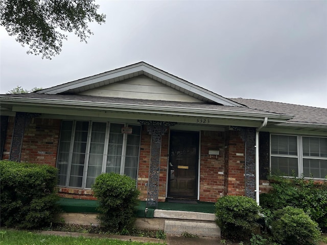 view of front facade featuring brick siding, roof with shingles, and covered porch