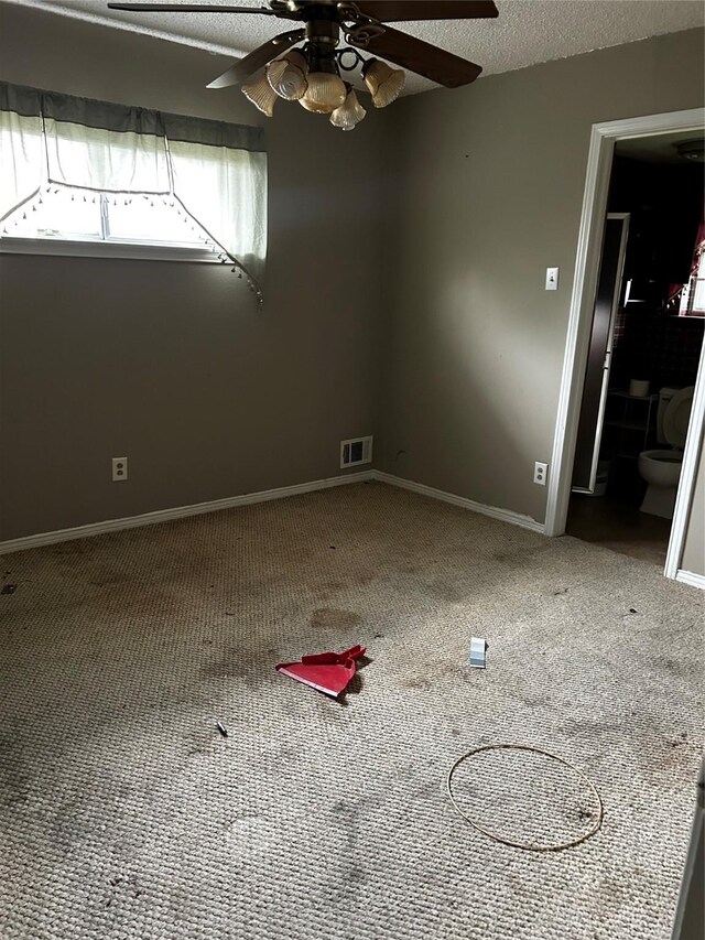 carpeted spare room with baseboards, ceiling fan, and visible vents