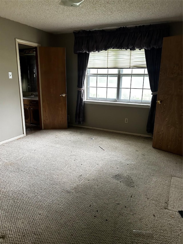 empty room with carpet floors, a textured ceiling, and baseboards