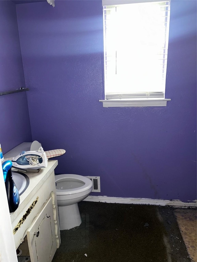 half bathroom with baseboards, toilet, and vanity