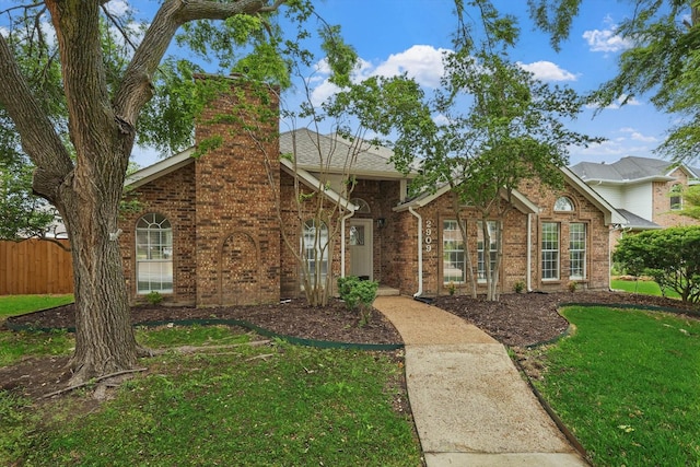 view of front of house featuring fence, a chimney, a front yard, and brick siding