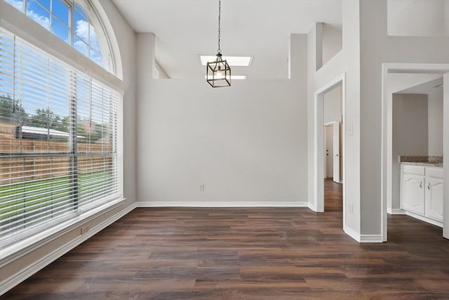 unfurnished dining area featuring baseboards, dark wood finished floors, and a towering ceiling