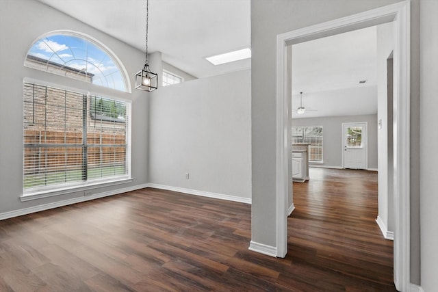 unfurnished dining area with baseboards, ceiling fan with notable chandelier, dark wood-style floors, and a skylight