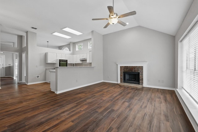 unfurnished living room with a healthy amount of sunlight, a fireplace, a ceiling fan, and dark wood-type flooring
