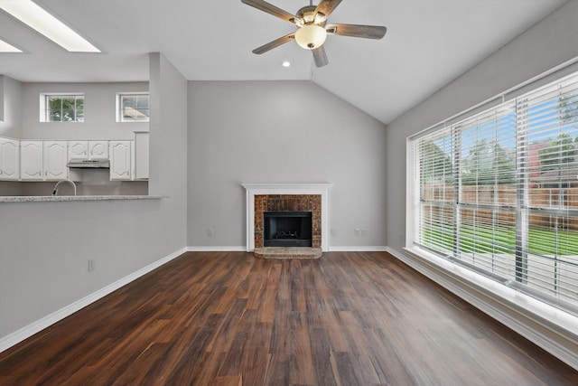 unfurnished living room featuring a ceiling fan, dark wood finished floors, a brick fireplace, and a healthy amount of sunlight