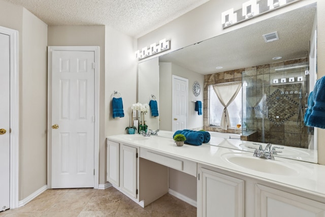 full bathroom featuring a sink, double vanity, a textured ceiling, a shower stall, and visible vents