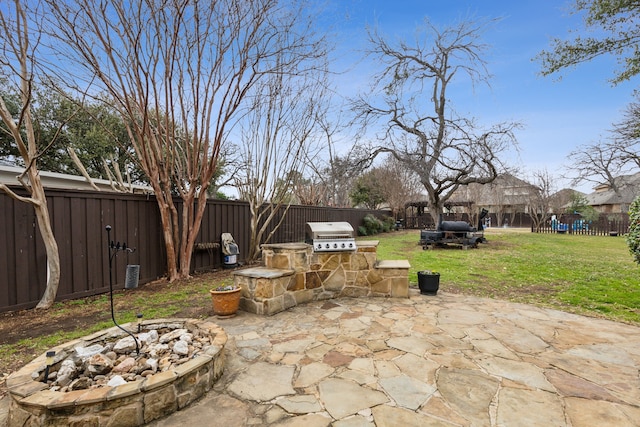 view of patio with exterior kitchen, an outdoor fire pit, a fenced backyard, a playground, and a grill