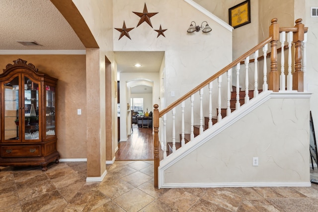 foyer featuring visible vents, arched walkways, stairway, baseboards, and ornamental molding