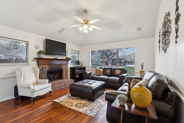 living area with ceiling fan, a brick fireplace, a textured ceiling, wood finished floors, and lofted ceiling