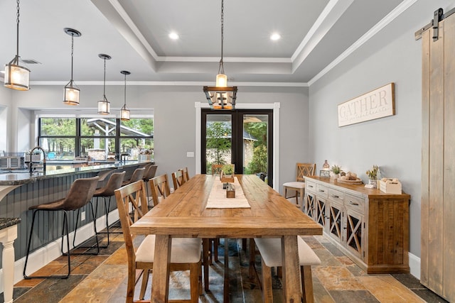 dining space featuring stone tile floors, a tray ceiling, a barn door, and a wealth of natural light