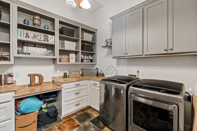 laundry room with ornamental molding, cabinet space, stone finish flooring, and washing machine and clothes dryer