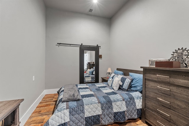bedroom with baseboards, wood finished floors, a barn door, and visible vents