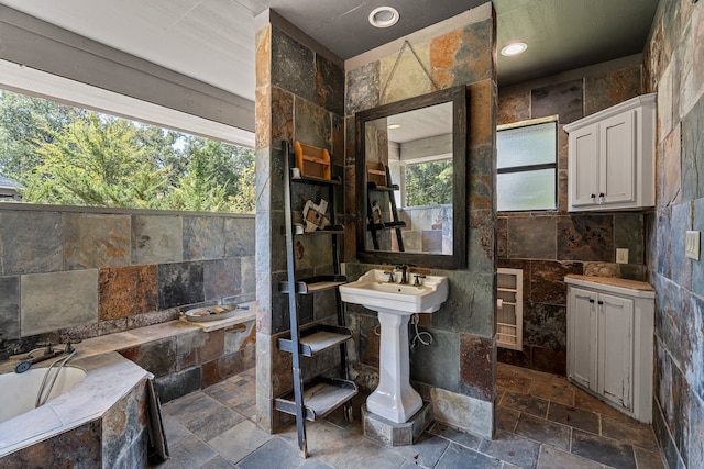 full bathroom featuring stone tile floors, tile walls, a healthy amount of sunlight, and a bath