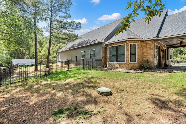 back of house featuring a yard, fence, a shingled roof, and stone siding