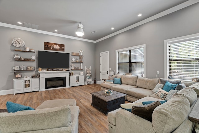 living room with crown molding, light wood-style floors, a glass covered fireplace, baseboards, and visible vents