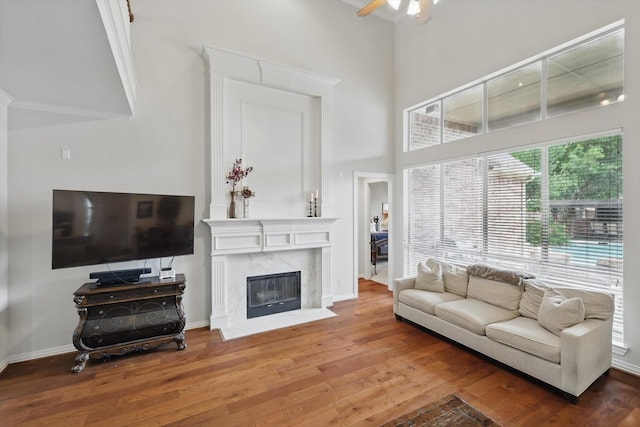 living area with a ceiling fan, a towering ceiling, a fireplace, wood finished floors, and baseboards