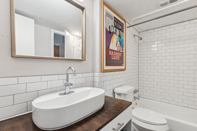 bathroom featuring toilet, tile walls, a textured ceiling, visible vents, and bathing tub / shower combination