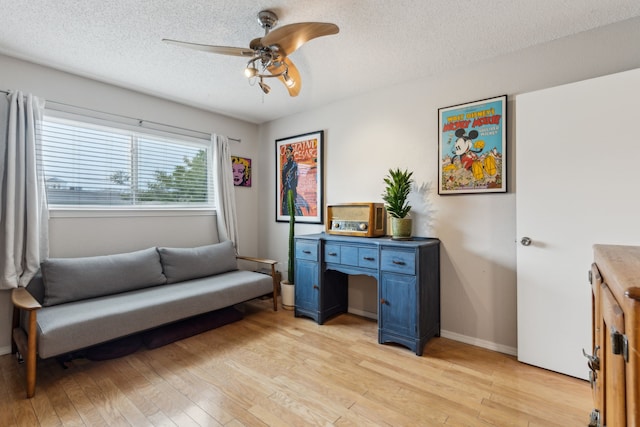 living area featuring light wood-type flooring, a textured ceiling, baseboards, and a ceiling fan