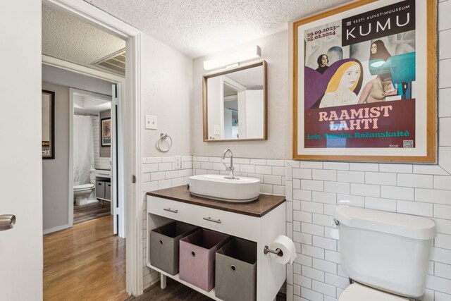 bathroom with toilet, tile walls, wood finished floors, vanity, and a textured ceiling