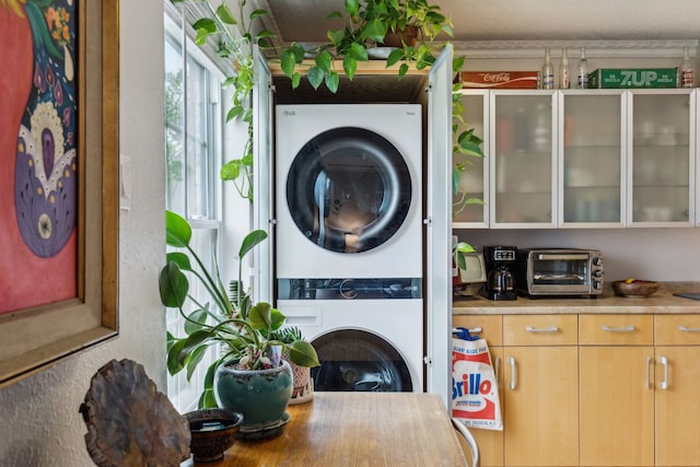 clothes washing area with laundry area, stacked washer and dryer, and a toaster