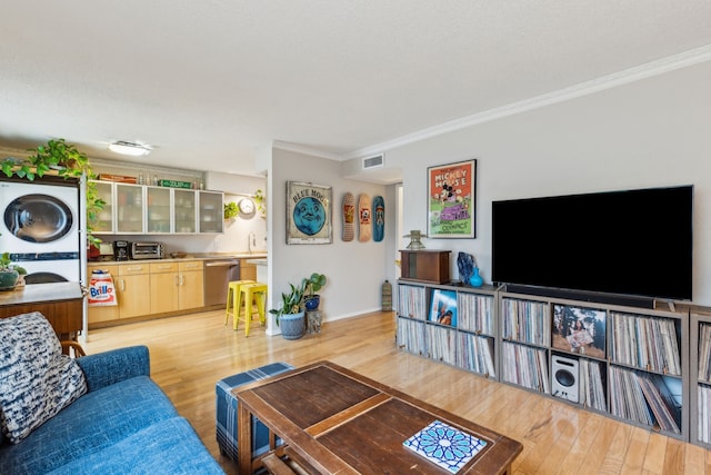 living area with stacked washer / dryer, ornamental molding, and light wood-style flooring