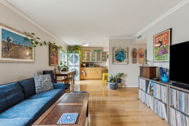 living room featuring light wood-style flooring, a textured ceiling, baseboards, ornamental molding, and visible vents