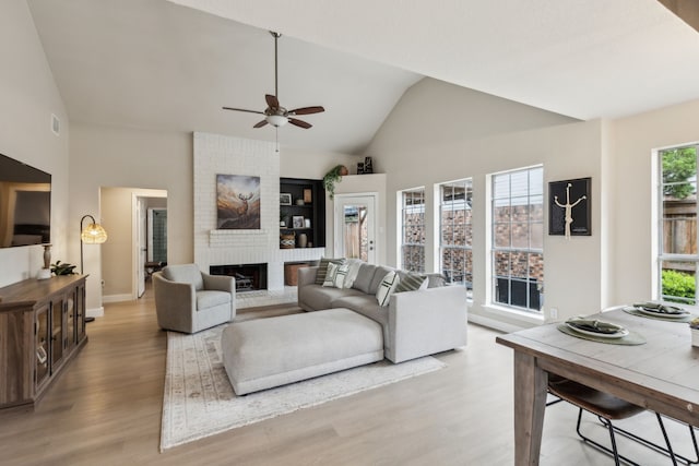living room featuring a fireplace, high vaulted ceiling, a ceiling fan, baseboards, and light wood-type flooring
