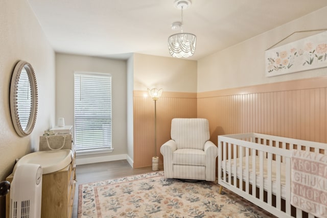 bedroom featuring an inviting chandelier, a wainscoted wall, wood finished floors, and a crib