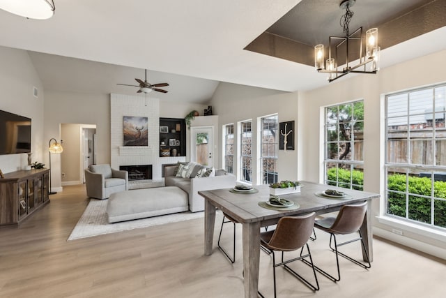 dining room with plenty of natural light, light wood-style flooring, a brick fireplace, and vaulted ceiling