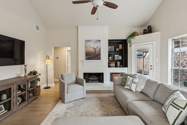 living room featuring ceiling fan, a brick fireplace, high vaulted ceiling, wood finished floors, and visible vents
