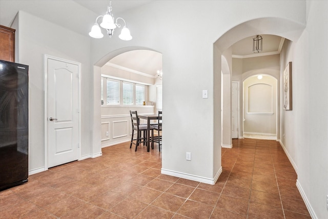 hall featuring tile patterned flooring, crown molding, baseboards, arched walkways, and a notable chandelier