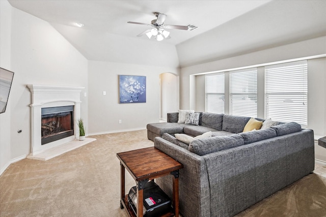 carpeted living area with visible vents, lofted ceiling, ceiling fan, a fireplace with raised hearth, and arched walkways