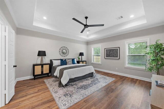 bedroom with a raised ceiling, ornamental molding, wood finished floors, and visible vents