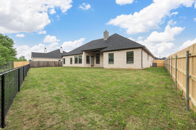 back of property featuring a lawn, a chimney, and a fenced backyard