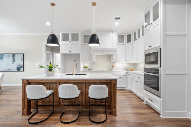 kitchen featuring visible vents, built in microwave, a sink, stainless steel oven, and an island with sink