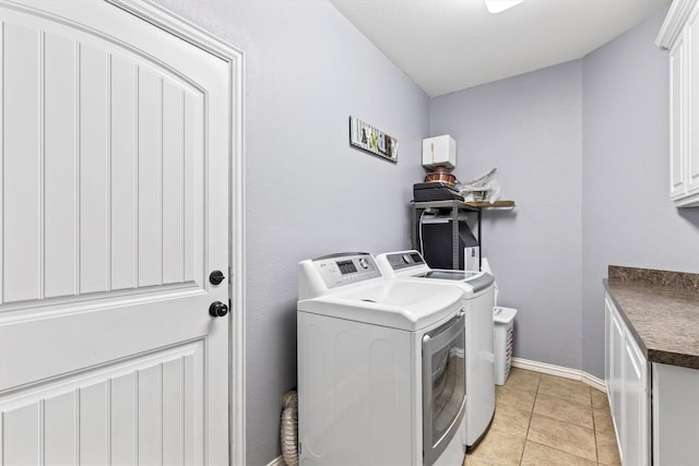 clothes washing area featuring light tile patterned floors, baseboards, washing machine and dryer, and cabinet space