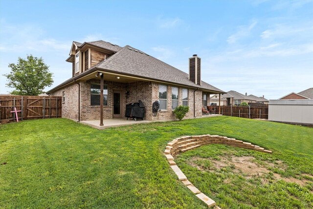 rear view of property with a fenced backyard, a chimney, brick siding, a patio area, and a yard