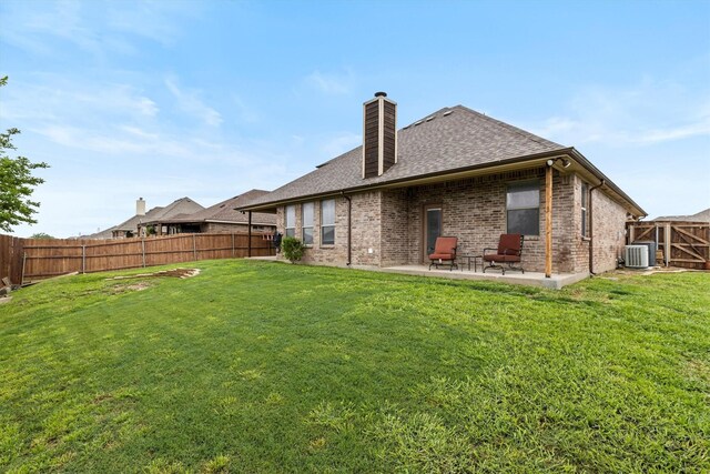 rear view of house with a chimney, a lawn, brick siding, a fenced backyard, and a patio