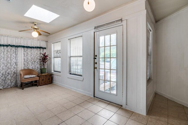 doorway to outside featuring a skylight, baseboards, light tile patterned floors, and a ceiling fan