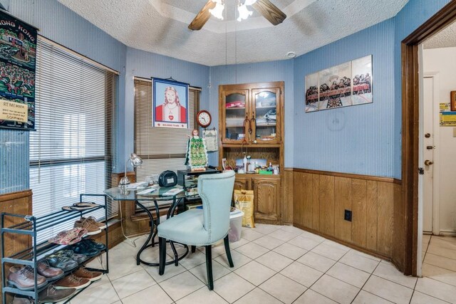 dining area featuring wooden walls, tile patterned flooring, a ceiling fan, and a textured ceiling