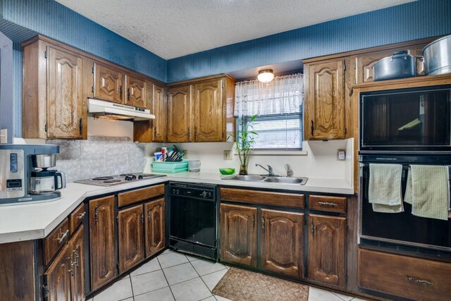 kitchen with a sink, under cabinet range hood, black appliances, and light countertops